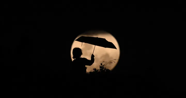 epaselect epa10293291 A child plays with an umbrella against the rising full moon ahead of a total lunar eclipse in Stanwell Park, Australia, 08 November 2022. A blood moon will be visible when a total lunar eclipse takes place later tonight. EPA/DEAN LEWINS AUSTRALIA AND NEW ZEALAND OUT/Dean Lewins