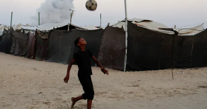 Palestinski dječak igra fudbal dok se dim diže nakon izraelskog napada u Khan Younisu/REUTERS/Foto: Hatem Khaled