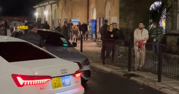 A wounded man walks on a sidewalk following a stabbing incident at a train station in Huntingdon, Britain, November 1, 2025, in this screengrab obtained from a social media video. @_ACC5_/via REUTERS THIS IMAGE HAS BEEN SUPPLIED BY A THIRD PARTY. MANDATORY CREDIT. NO RESALES. NO ARCHIVES. THIS IMAGE WAS PROCESSED BY REUTERS TO ENHANCE QUALITY. AN UNPROCESSED VERSION HAS BEEN PROVIDED SEPARATELY. VERIFICATION: Reuters was able to confirm the location and date of the footage by original file metadata from the source./@_acc5_