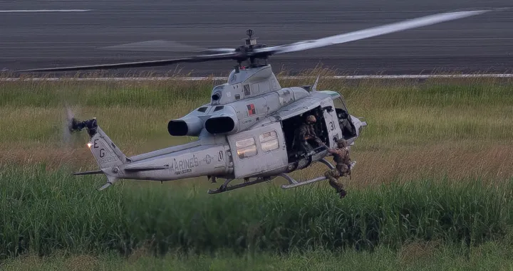 A U.S. military service member hangs from a U.S. Marine Corps UH-1Y Venom helicopter as it hovers over a taxiway during a training exercise at the former Roosevelt Roads naval base in Ceiba, Puerto Rico, December 22, 2025. REUTERS/Ricardo Arduengo/Ricardo Arduengo