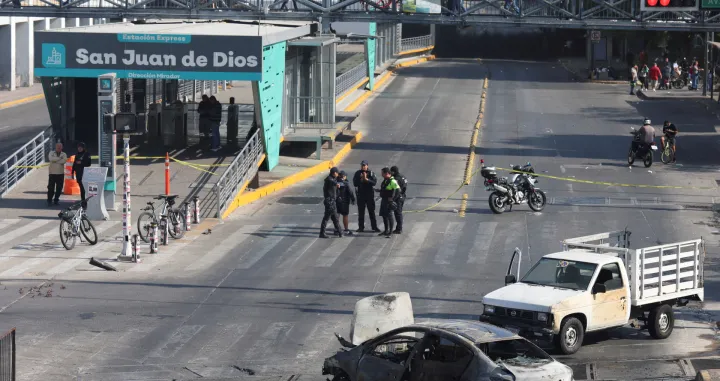 Police officers and civilians walk near the burned wreckage of a vehicle used as a barricade by members of organized crime following a series of detentions by federal forces, in Guadalajara, Mexico, February 22, 2026. REUTERS/Michelle Freyria REFILE - UPDATING SLUG/Michelle Freyria