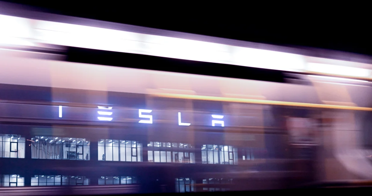 epa10387461 The Tesla logo seen through a window of a bus passing in front of the Tesla Gigafactory in Gruenheide near Berlin, Germany, 03 January 2023. The Tesla Gigafactory Berlin-Brandenburg plant in Gruenheide produces 2,000 Model Y electric cars in a week. EPA/Filip Singer/Filip Singer